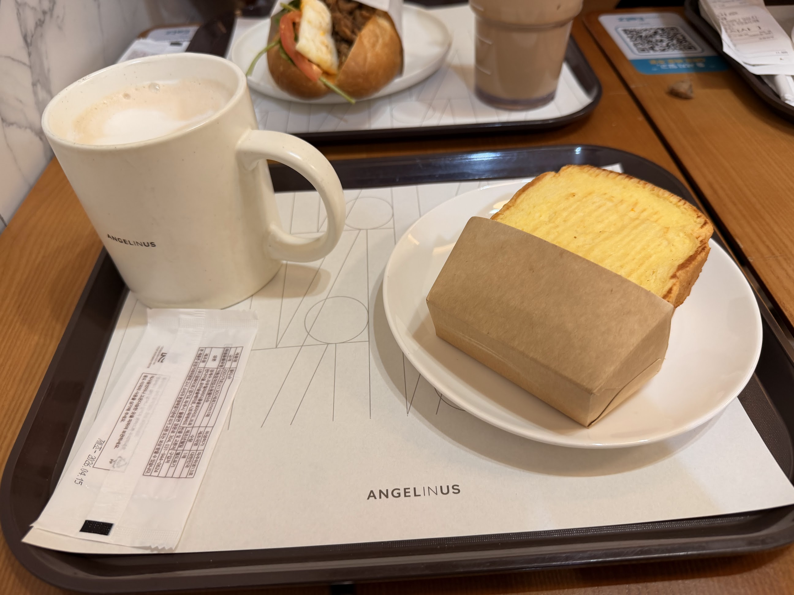 明洞のANGELINUSでの朝ご飯。白いマグカップと厚切りのトースト、奥にはサンドイッチとドリンクが並んでいる