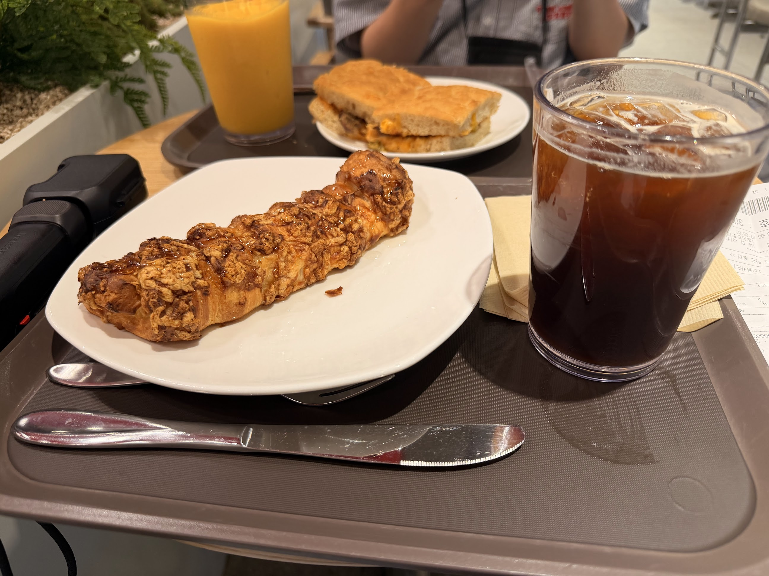 HOLLYSでの朝食。白い皿に載ったパンとアイスコーヒー、奥にはサンドイッチとオレンジ色のドリンクが並んでいる