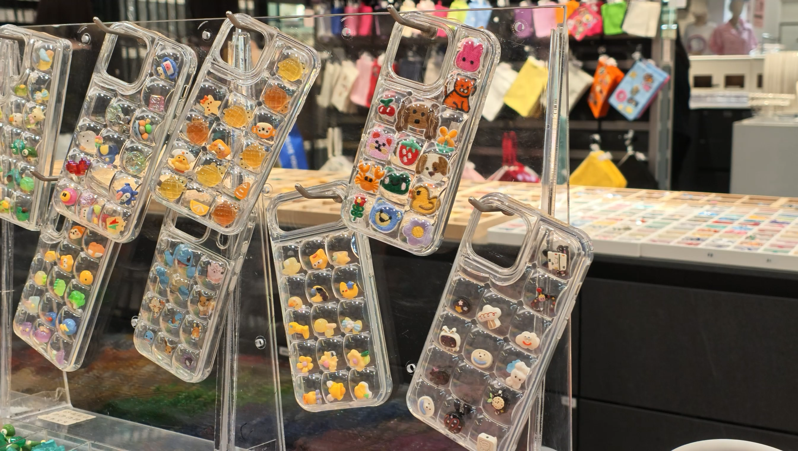 MIMILINEの店頭に並ぶ透明なスマホケース。小さな区画に動物や花、お菓子などのカラフルなパーツが入っている