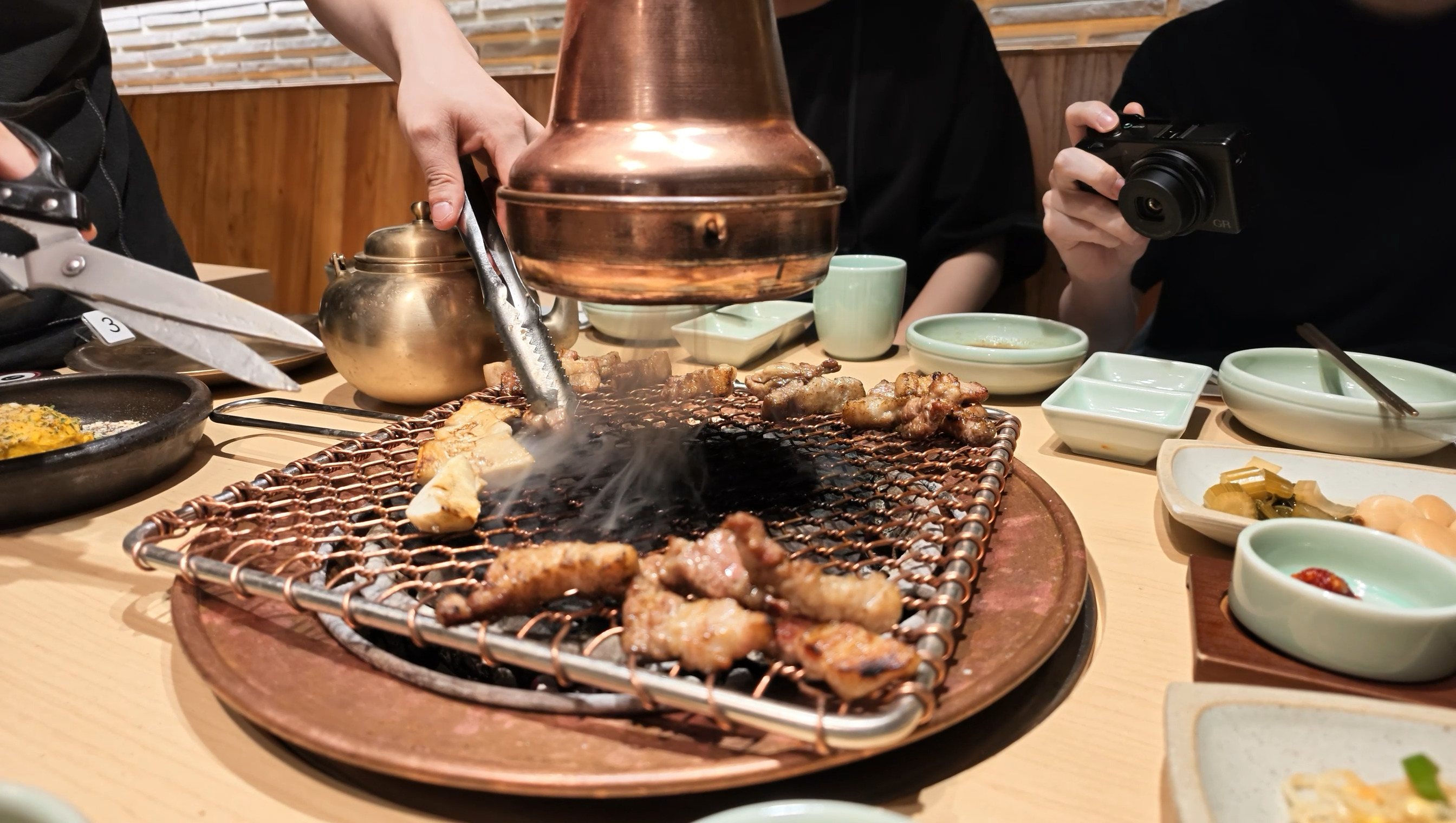 王妃家 明洞本店のサムギョプサル。網の上で焼かれた肉をハサミとトングで切り分けている様子