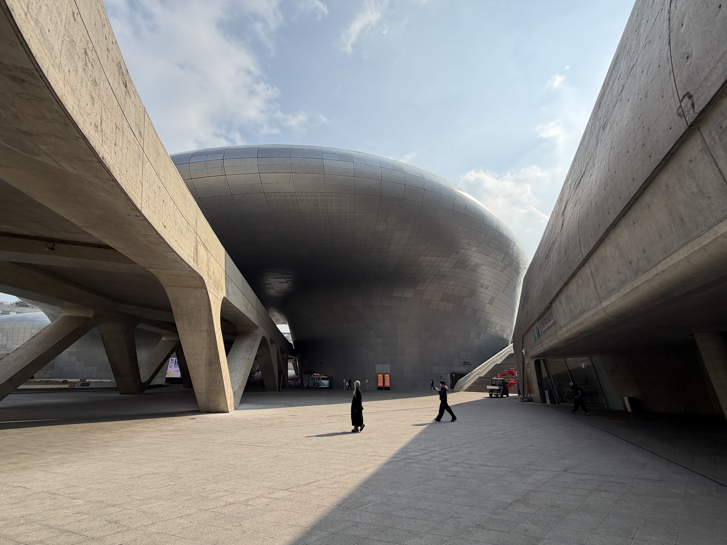 ザハ・ハディッド設計の東大門デザインプラザ(DDP)の全景。コンクリートの柱が斜めに伸び、銀色の巨大な曲面建築が空に浮かぶように佇んでいる