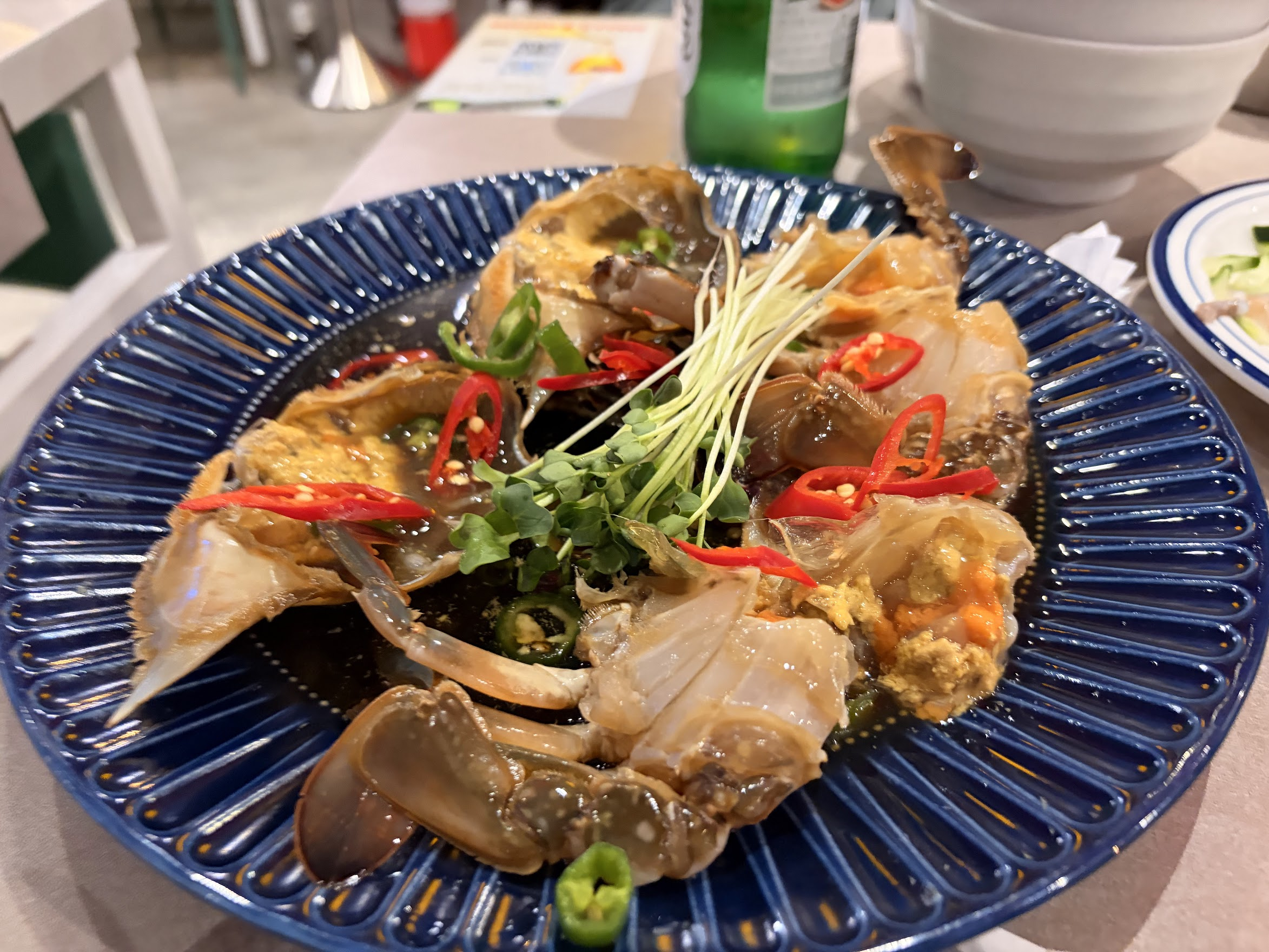 青い皿に美しく盛り付けられたカンジャンケジャン。醤油ダレに漬けられたワタリガニの上に赤い唐辛子とパクチー、白髪ネギがあしらわれている