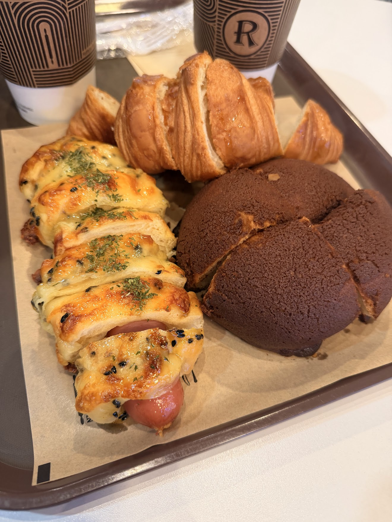 DDPのパン屋さんで買ったパンのトレー。ツヤツヤに焼き上がったチーズのせソーセージパン、バターの香るクロワッサン、しっとりしたチョコレートパンが並ぶ。韓国のパンは表面がとにかくツヤツヤ