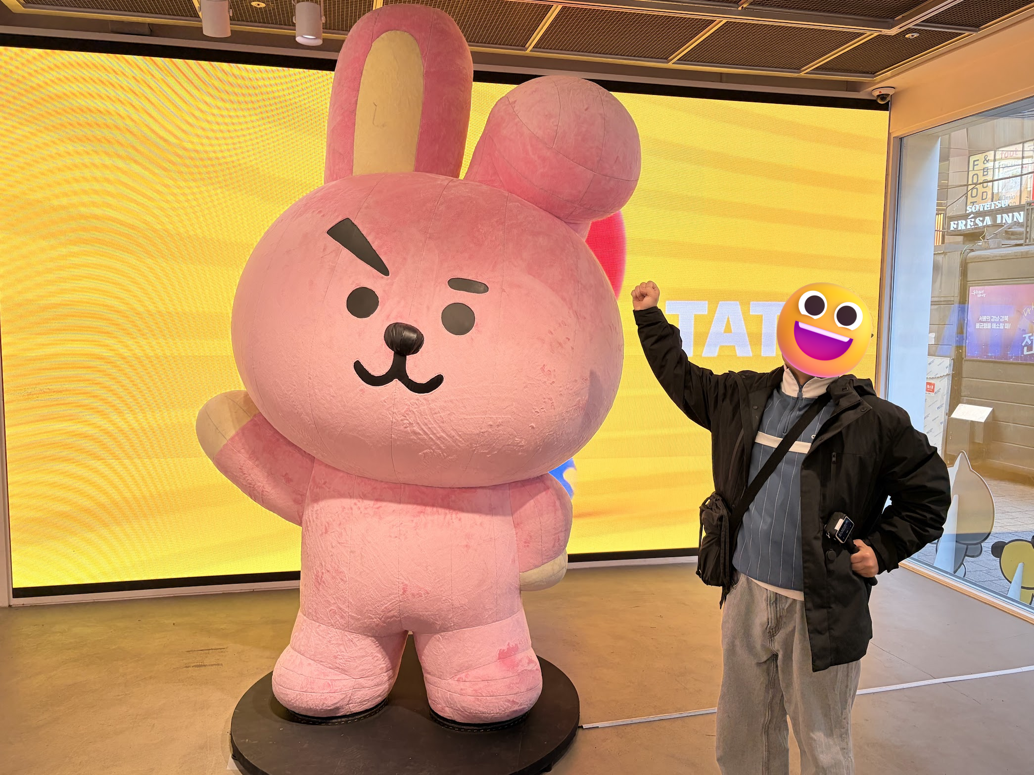 LINE FRIENDSストアに展示されているピンクのうさぎキャラクターCOOKYの等身大フィギュアの横で、同じポーズをとって記念撮影。背景は黄色のスクリーン