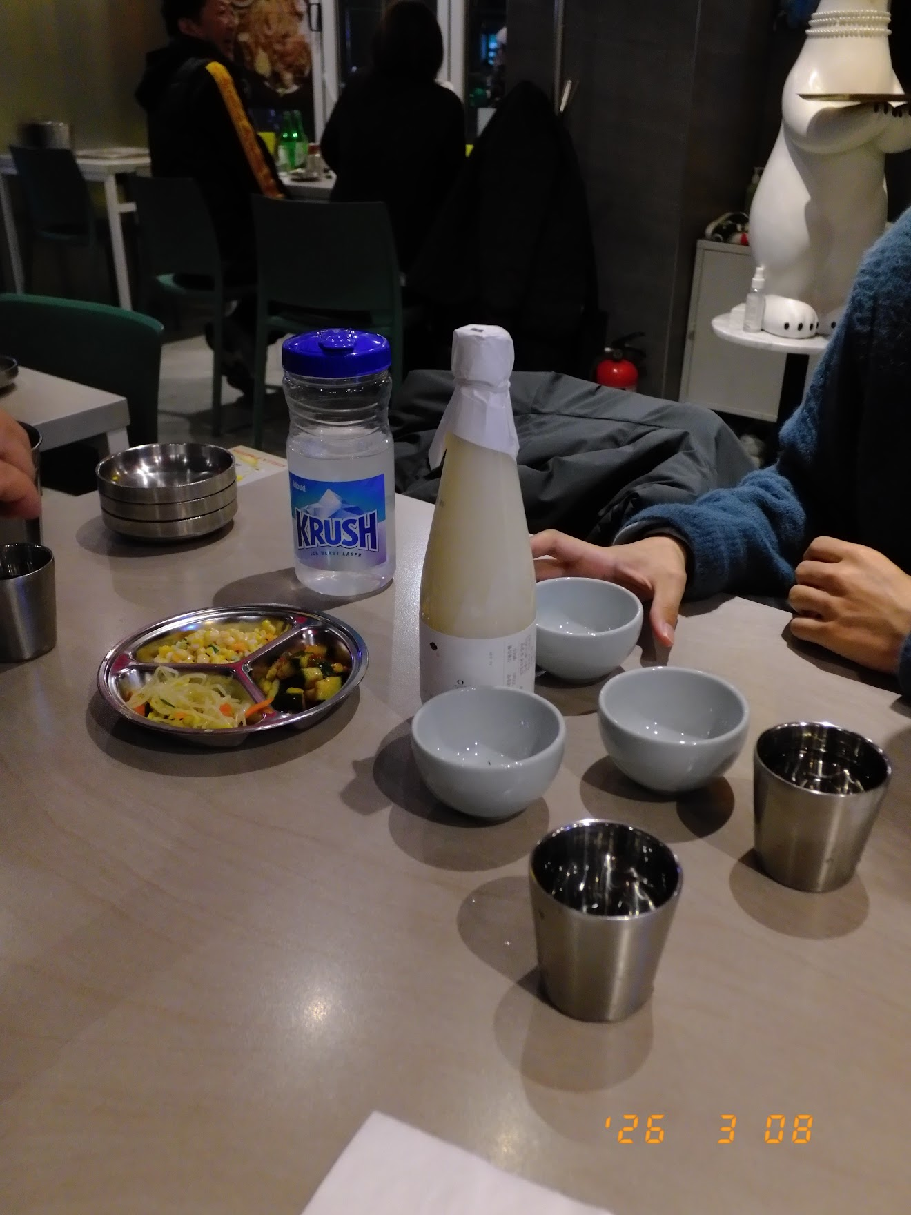 テーブルに並ぶ白い生マッコリの瓶とKRUSHビール、おちょこやステンレスのコップ。これからの海鮮ディナーに備えて乾杯準備