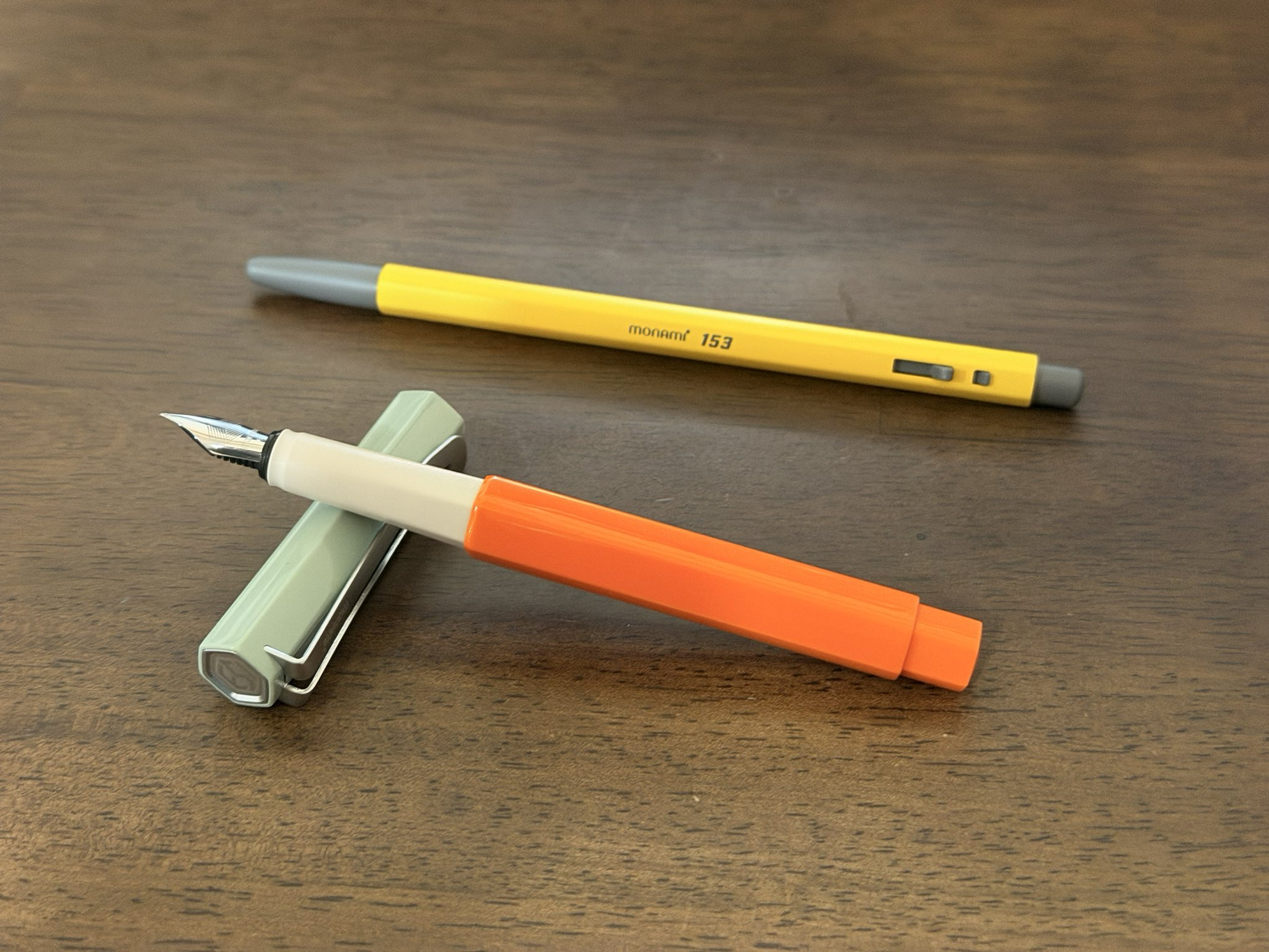 聖水のmonamiストアで購入したオレンジ色の万年筆と黄色のmonami 153ボールペン。木のテーブルの上にキャップを外した状態で並べて撮影