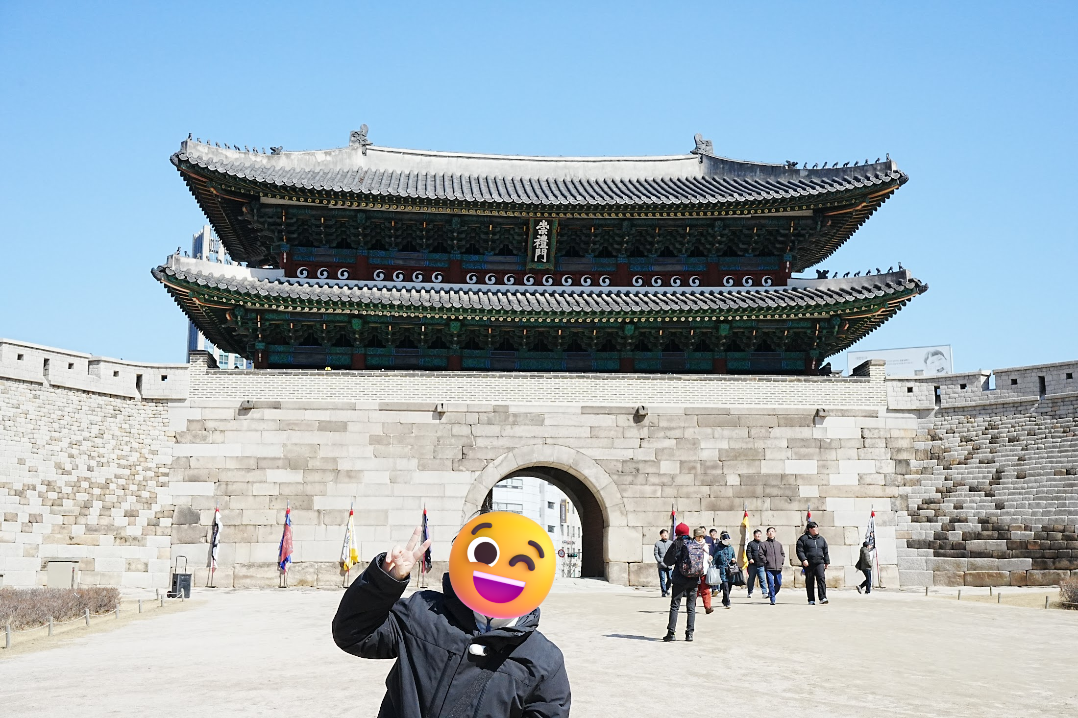 青空の下、堂々とそびえる南大門(崇礼門)の石造りの門の前でピースサインをして記念撮影