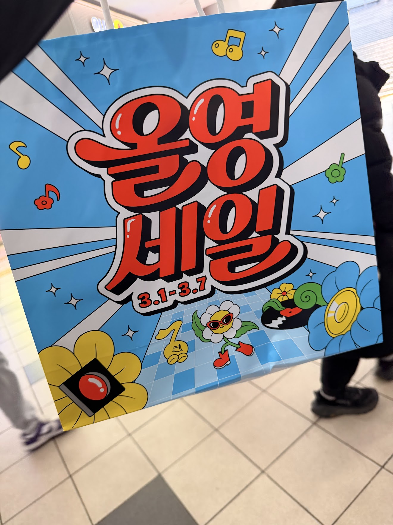 オリーブヤングの「올영세일(オリヨンセール)」と書かれたポップで可愛い水色の紙袋。花やキャラクターのイラスト入り