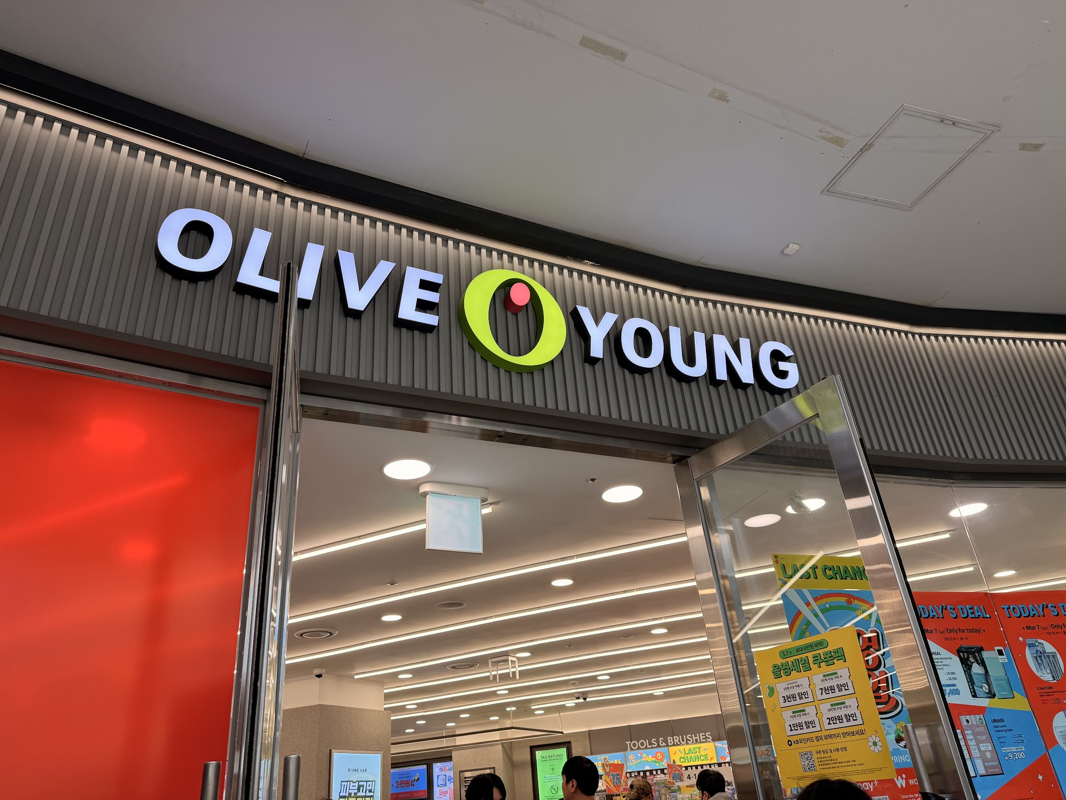 ソウル駅地下にあるオリーブヤングの店舗入口。白と緑のロゴが大きく掲げられ、店頭にはセールのポスターが並んでいる