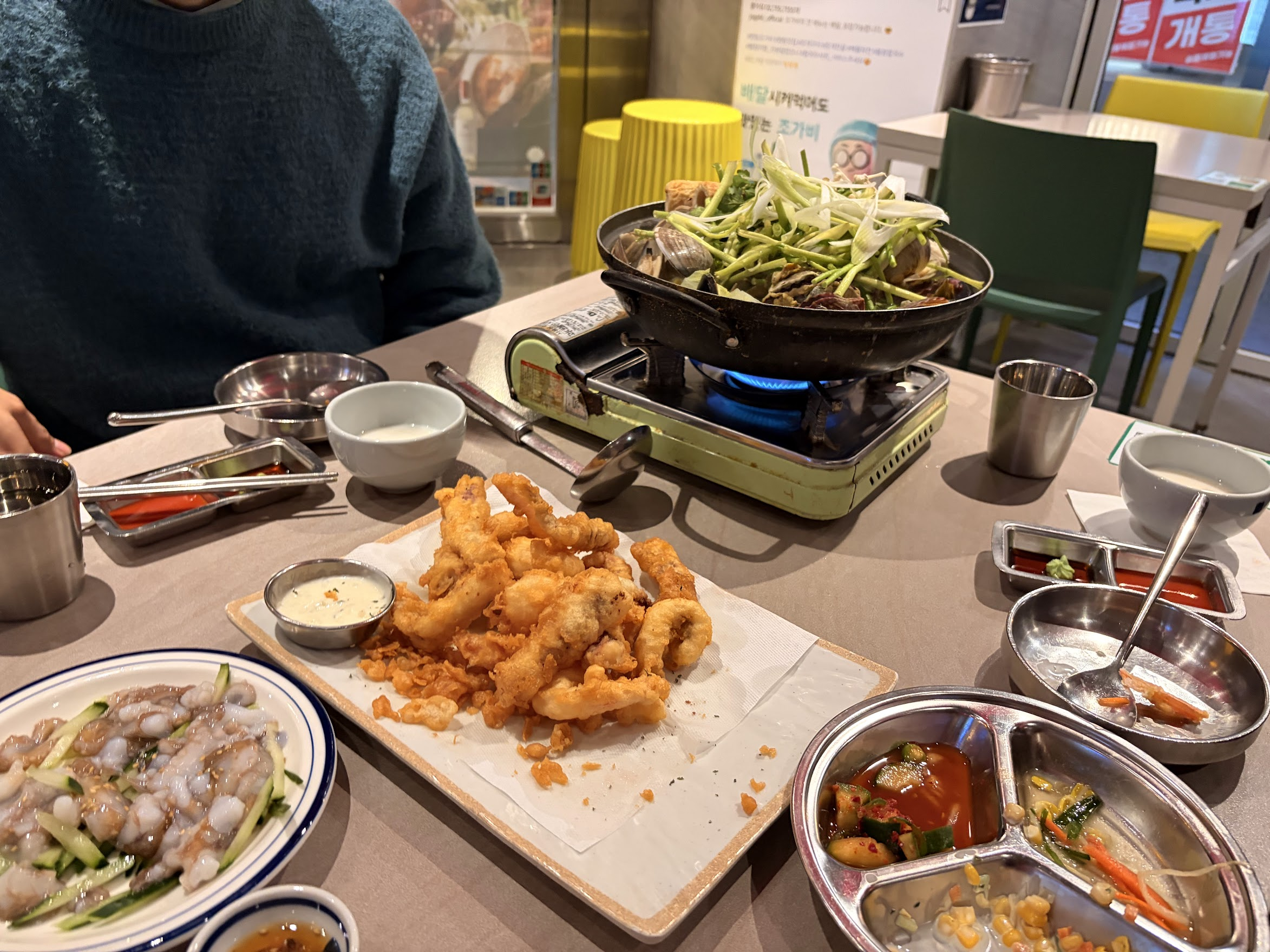 Jogabi Seafood Barのテーブルいっぱいに並ぶ海鮮料理。手前にはまだ動いている活タコの刺身と衣がサクサクの海鮮フライ、奥ではネギたっぷりの貝鍋がコンロの上でグツグツ煮えている